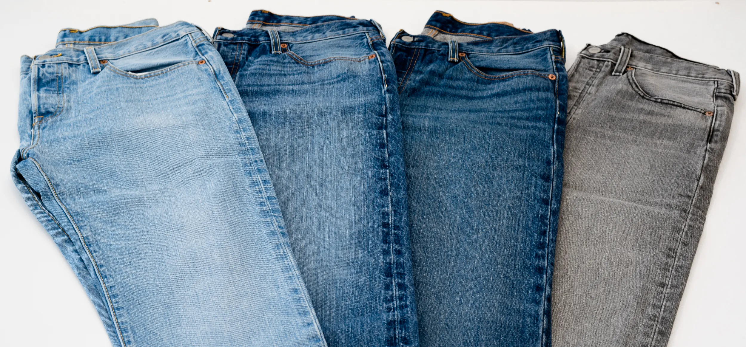 Four pairs of jeans laid side by side, from light bleached blue to dark grey